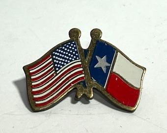 May include: A vintage metal pin featuring the flags of the United States and Texas. The American flag has red and white stripes with a blue field of white stars. The Texas flag has a white star on a blue background, with white and red stripes.