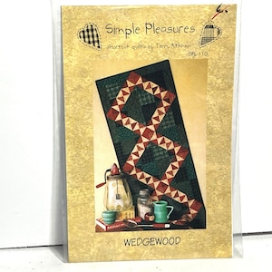 Könnte beinhalten: Eine Packung für ein Quiltmuster mit dem Titel "Simple Pleasures" von Terry Atkinson. Das Muster zeigt ein geometrisches Design in Rot-, Grün- und Cremefarben. Das Wort "WEDGEWOOD" ist unten auf der Packung aufgedruckt.