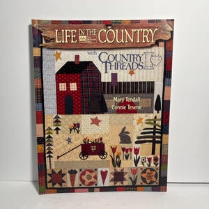 May include: A book titled "Life in the Country" with "Country Threads" on the cover. The cover features a patchwork design with a red house, stars, a bunny, and a cart filled with flowers. The authors are Mary Tendall and Connie Tesene.