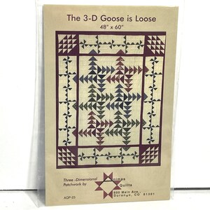 May include: A tan paper package with the text "The 3-D Goose is Loose" and "48" x 60"" (approx. 122cm x 152cm) printed on it. The package features a quilt pattern with geometric shapes in shades of blue, burgundy, and cream. The package also includes the text "Three-Dimensional Patchwork by" and the name of the quilt maker.