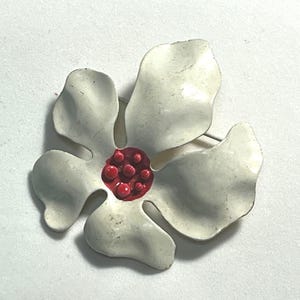 May include: White enamel flower brooch with a red center. The center has a textured, bumpy surface.