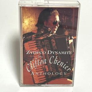 May include: A cassette tape case with a photo of Clifton Chenier playing an accordion. The text on the case reads "Zydeco Dynamite The Clifton Chenier Anthology".