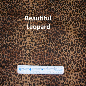 May include: Brown fabric with a black leopard print pattern. The fabric has a subtle sheen and a soft texture. The text "Beautiful Leopard" is printed in white on the fabric.