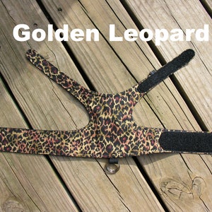 May include: A golden leopard print dog harness with black adjustable straps and a metal ring. The harness is made of fabric and has a velcro closure.