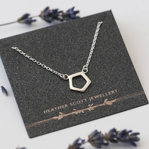 May include: A silver necklace with a geometric hexagon pendant. The necklace is displayed on a black card with the text "Heather Scott Jewellery".