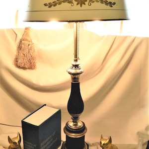 May include: A vintage table lamp with a cream-colored lampshade adorned with floral designs. The lamp features a black base with brass accents and a decorative tassel. A book titled "History of Western Civilization" and two golden cat figurines are also present.