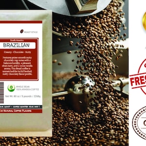 May include: A brown paper bag with a label that reads "Smokin Beans" and "Brazilian" coffee. The label describes the coffee as "Creamy-Chocolate-Nutty" and features a green leaf with the text "Whole Bean 100% Arabica Coffee". The bag is sitting on a pile of roasted coffee beans.