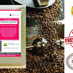 May include: A brown paper bag with a colorful design and the text "Smokin Beans Specialty Coffee Roastery" and "Ethiopia Sidamo" printed on it. The bag contains 32 ounces of whole bean 100% Arabica coffee. The bag is sitting on a table with a metal scoop and coffee beans.