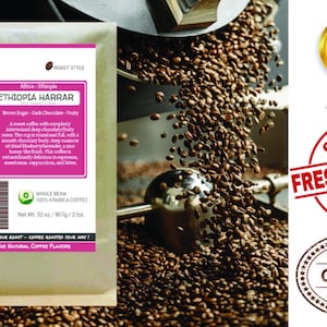 May include: A brown paper bag of Ethiopia Harrar coffee beans with a pink label that reads "Ethiopia Harrar" and describes the coffee as having notes of brown sugar, dark chocolate, and fruit. The bag is sitting on a pile of roasted coffee beans. The label also states that the coffee is 100% Arabica and has a net weight of 32 ounces.