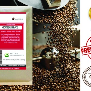 May include: A brown paper bag with a label that reads "Smokin Beans Specialty Single Beans Honduras" and features a red apple, cherry, and milk chocolate design. The label also states "Whole Bean 100% Arabica Coffee" and "Net Wt. 80 oz / 5 pounds / 2268g". The bag is in front of a coffee roaster with coffee beans pouring out.