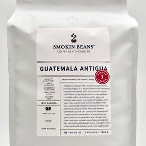 May include: A white stand-up pouch of Smokin Beans Guatemala Antigua coffee. The label features the brand name, product origin, flavor notes of chocolate, caramel, and nutmeg, and technical details including 100% Arabica and a net weight of 80 oz.