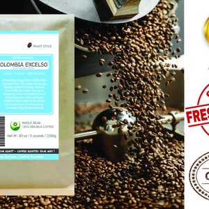 May include: A brown paper bag with a blue and white label that reads "Smokin Beans Specialty Coffee Roasting" and "Colombia Excelso". The label also includes a description of the coffee and its origin. The bag is sitting on a pile of roasted coffee beans.