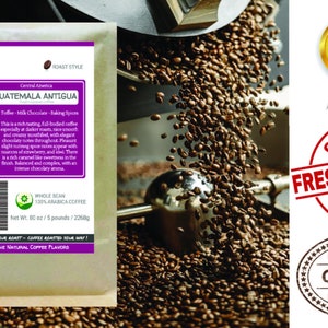 May include: A bag of whole bean Guatemala Antigua coffee with a brown and green label. The label reads "Smokin Beans Specialty Coffee Roastery" and "Guatemala Antigua" with a description of the coffee's flavor profile. The bag is sitting on a pile of roasted coffee beans.