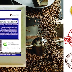 May include: A brown paper bag with a white label that reads "Smokin Beans Specialty Coffee Roastery" and "Brazil Peaberry". The label also includes a description of the coffee's flavor profile, which is "Creamy - Dark Chocolate - Hazelnut". The bag is sitting on a pile of roasted coffee beans.