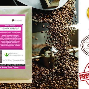 May include: A brown paper bag with a white label that reads "Smokin Beans Specialty Coffee Roasting" and "Ethiopia Harrar" with a description of the coffee beans. The bag is sitting on a table with a coffee roaster in the background.