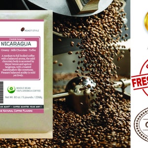 May include: A brown paper bag with a white label featuring the text "Smokin Beans Specialty Coffee Roastery" and "Nicaragua" in a red and white banner. The label also includes a description of the coffee's flavor profile and origin. The bag is sitting on a pile of roasted coffee beans.