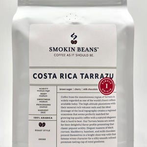 May include: A white coffee bag featuring the Smokin Beans logo and text Costa Rica Tarrazu. The label lists flavor notes of brown sugar, cherry, and milk chocolate, specifies 100% Arabica, and states a net weight of 32 ounces or 2 pounds.