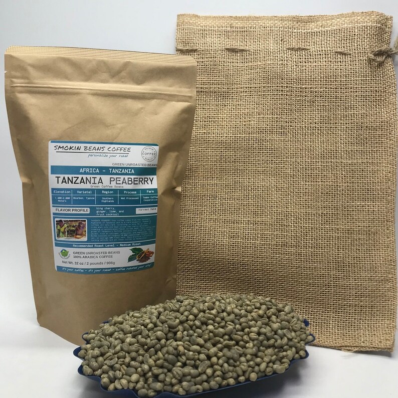 May include: A brown paper bag with a label that reads "Smokin Beans Coffee" and "Tanzania Peaberry" green coffee beans. The bag is sitting on a burlap sack. The coffee beans are in a blue bowl.
