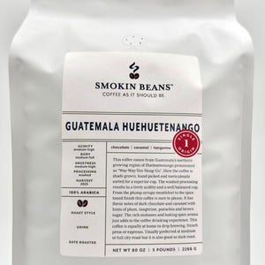 May include: A white stand-up pouch of Smokin Beans Guatemala Huehuetenango coffee. The label features the brand name, origin, flavor notes of chocolate, caramel, and tangerine, and specifies a net weight of 80 ounces, 5 pounds, or 2268 grams.