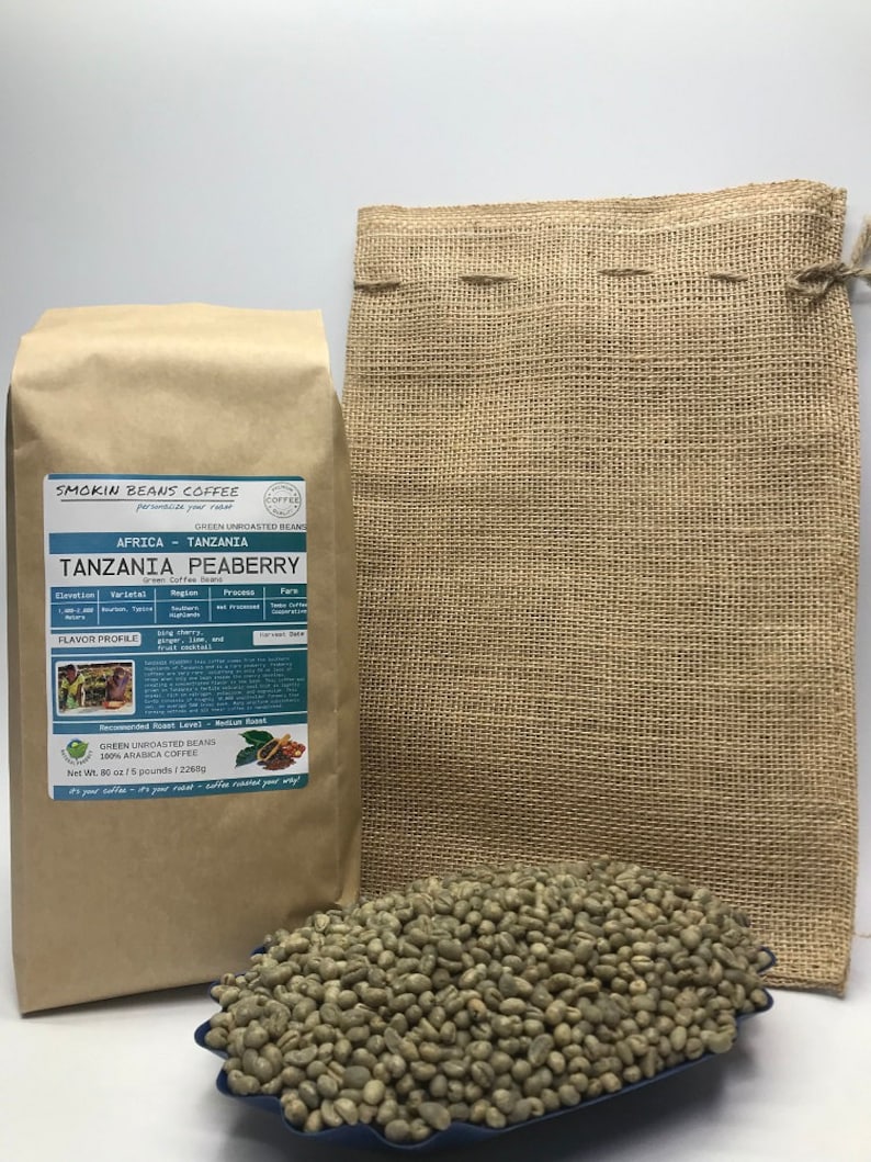 May include: A brown paper bag with the text "Smokin Beans Coffee" and "Tanzania Peaberry" on it. The bag contains green unroasted coffee beans. The beans are also shown in a blue bowl and a burlap sack.
