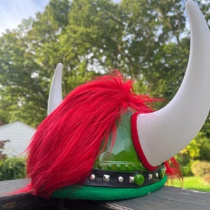 May include: Green and white Viking helmet with red fur. The helmet has a black band with silver studs and a green jewel.