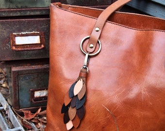 May include: A brown leather tote bag with a key chain featuring a multi-colored leather tassel. The bag has a top zipper closure and a long strap.