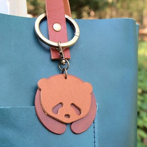 May include: A teal leather tote bag with a brown leather strap and a key chain featuring a brown leather panda charm.