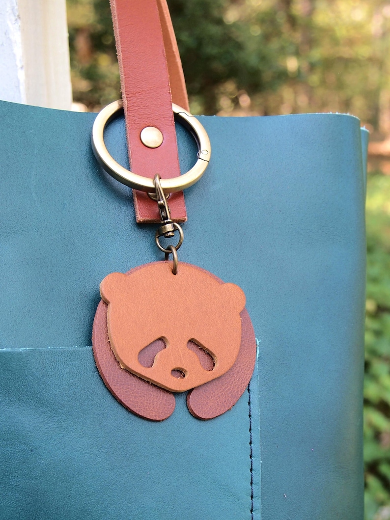 May include: A teal leather tote bag with a brown leather strap and a key chain featuring a brown leather panda charm.
