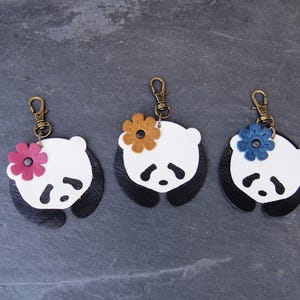 May include: Three leather panda keychains with different colored flower accents. The pandas are white with black ears and eyes, and the flowers are pink, yellow, and blue.