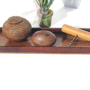 Puede incluir: Una bandeja de madera con una cesta tejida, una esfera de madera y un sacacorchos. El sacacorchos tiene el texto "GOODRICH & MURIES" impreso. La bandeja y los objetos est&aacute;n sobre un fondo blanco.