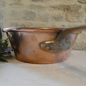 May include: A large copper pot with a long handle. The pot is sitting on a white surface.