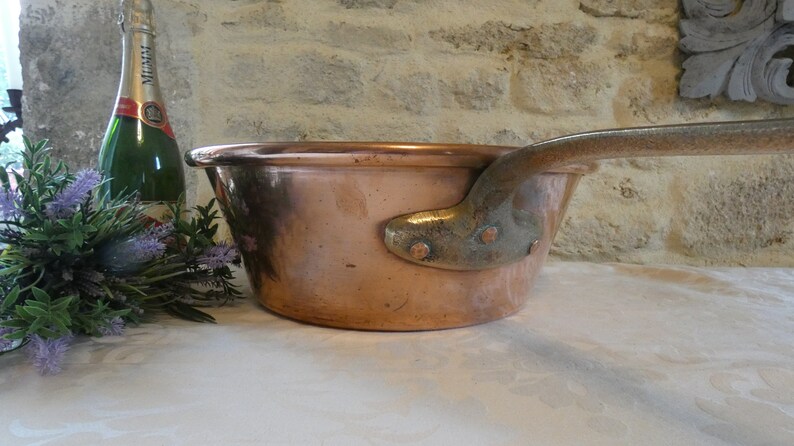 May include: A large copper pot with a long handle. The pot is sitting on a white surface.
