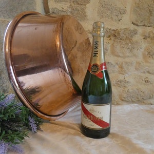 May include: A large copper bowl sits on a white tablecloth next to a bottle of Mumm champagne. A small bouquet of lavender is in the foreground.