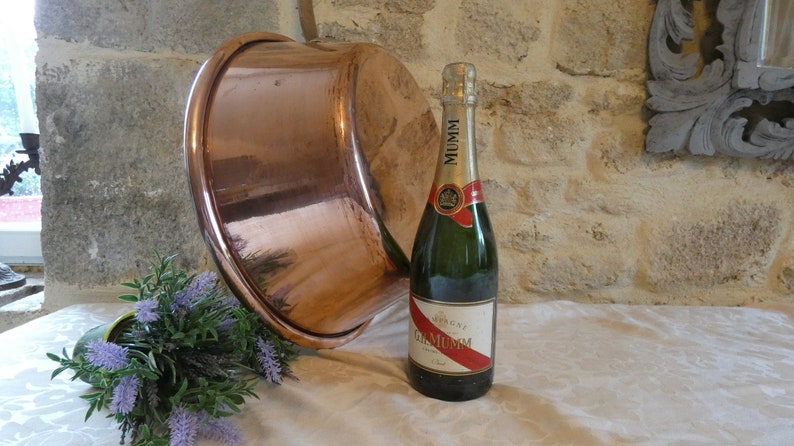 May include: A large copper bowl sits on a white tablecloth next to a bottle of Mumm champagne. A small bouquet of lavender is in the foreground.