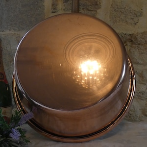 May include: The bottom of a large, copper pot with a shiny, reflective surface. The pot is sitting on a stone surface.