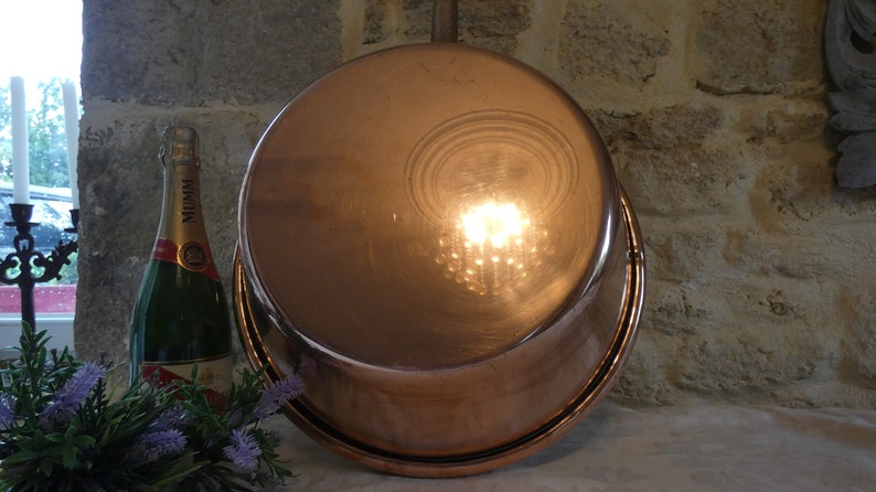 May include: The bottom of a large, copper pot with a shiny, reflective surface. The pot is sitting on a stone surface.