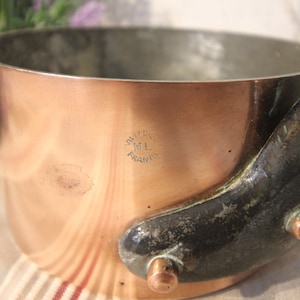 May include: Copper saucepan with a dark handle and rivets. The pot has a shiny copper exterior and a silver interior. The handle is dark with a curved shape. The pot has the text "Villedieu ML France" stamped on the side.