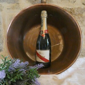 May include: A copper bowl with a bottle of champagne inside. The bowl is sitting on a white tablecloth. There is a bouquet of lavender flowers in the foreground.