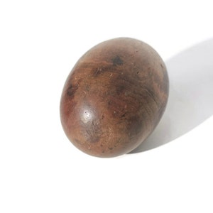 Puede incluir: Objeto de madera ovalado y liso, de color marr&oacute;n con vetas oscuras y visibles. La superficie parece pulida. El objeto est&aacute; sobre un fondo blanco, con una sombra a la derecha.