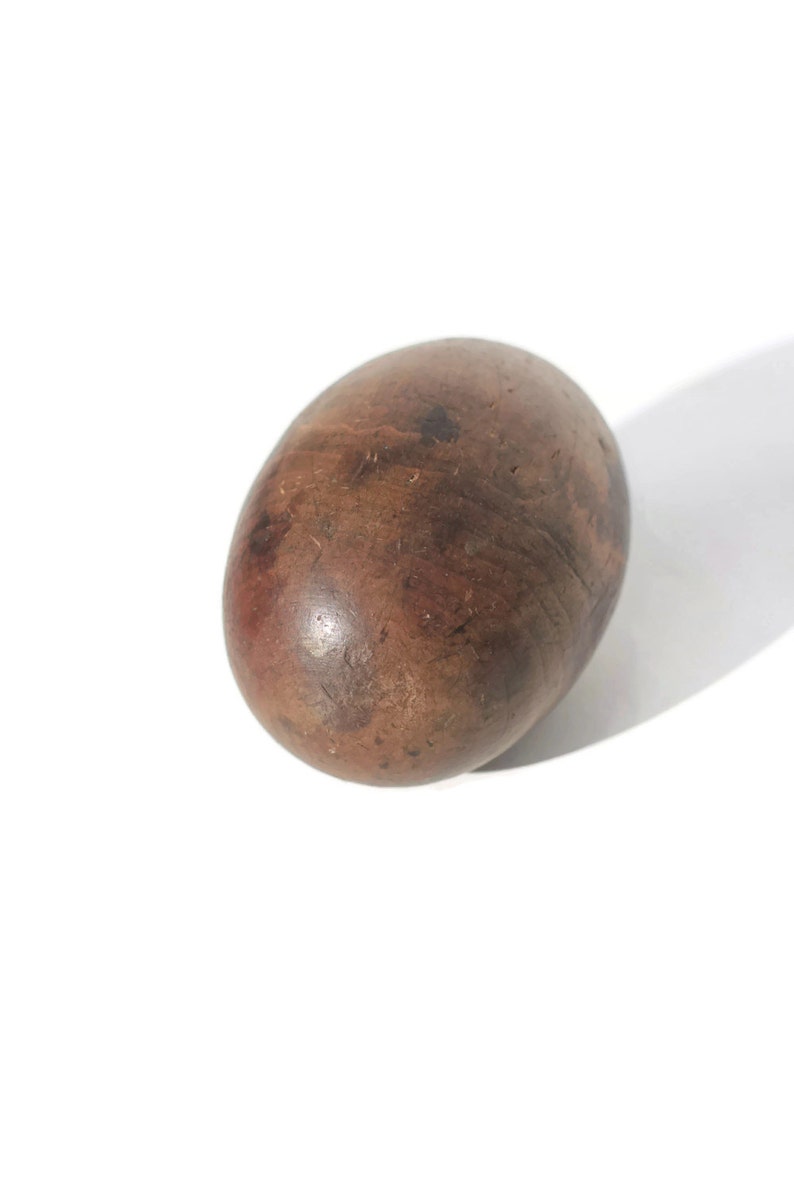 Puede incluir: Objeto de madera ovalado y liso, de color marr&oacute;n con vetas oscuras y visibles. La superficie parece pulida. El objeto est&aacute; sobre un fondo blanco, con una sombra a la derecha.