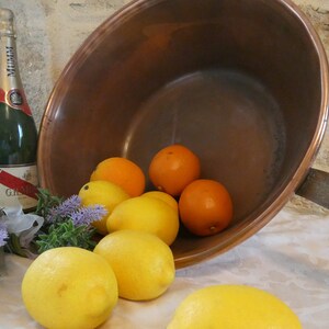 May include: A copper pot with a long handle, filled with lemons and oranges. A bottle of champagne is in the foreground, next to a bouquet of lavender.
