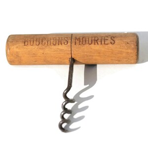 Puede incluir: Un sacacorchos vintage con mango de madera y gusano de metal. El mango es de color marr&oacute;n claro con las palabras "BOUCHONS MOURIES" impresas. La hoja es plateada. El sacacorchos est&aacute; dise&ntilde;ado para quitar corchos de botellas de vino.
