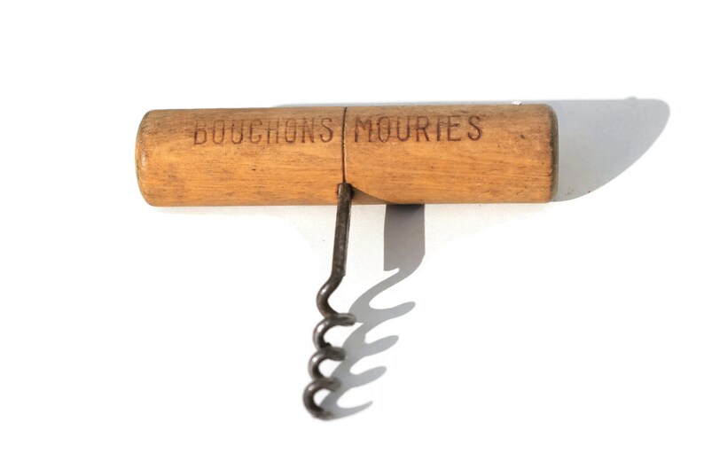 Puede incluir: Un sacacorchos vintage con mango de madera y gusano de metal. El mango es de color marr&oacute;n claro con las palabras "BOUCHONS MOURIES" impresas. La hoja es plateada. El sacacorchos est&aacute; dise&ntilde;ado para quitar corchos de botellas de vino.