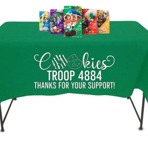 May include: A green tablecloth with the text "Cookies TROOP 4884 THANKS FOR YOUR SUPPORT!" and several boxes of cookies. The table is supported by black metal legs. The cookie boxes have various designs.