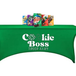 May include: Green table cover with the text "Cookie Boss Troop 87389" in white. There are several boxes of Girl Scout cookies on the table.