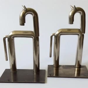 May include: A pair of silver metal bookends shaped like stylized horses. The horses are standing on rectangular bases.