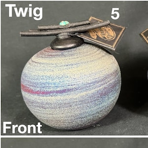 May include: Two spherical ceramic ornaments labeled 5 and 6, featuring a textured, multi-colored gradient finish. Each piece is topped with a dark, twig-like decorative element and a small turquoise accent. The items are shown from front and back.