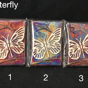 May include: Three ceramic tiles with a white butterfly design on a colorful background. The tiles are labeled 1, 2, and 3.