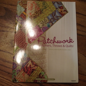 May include: A book titled "Patchwork Comforters, Throws & Quilts" with a colorful patchwork design on the cover. The book is published by Designs by White Birches and has the number 144059 on the bottom right corner.