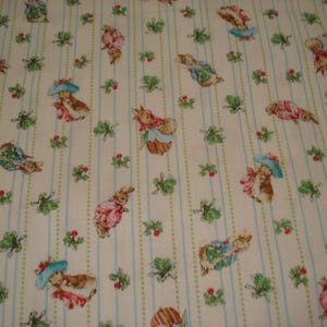 May include: A cream-colored fabric featuring a repeating pattern of rabbits in blue hats and red jackets, interspersed with small green leafy sprigs and red berries, all arranged between vertical light blue and dotted green stripes.
